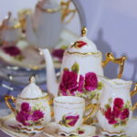 Conjunto de porcelana fina com flores vermelhas e dourado, incluindo bule, xícaras e leiteira
