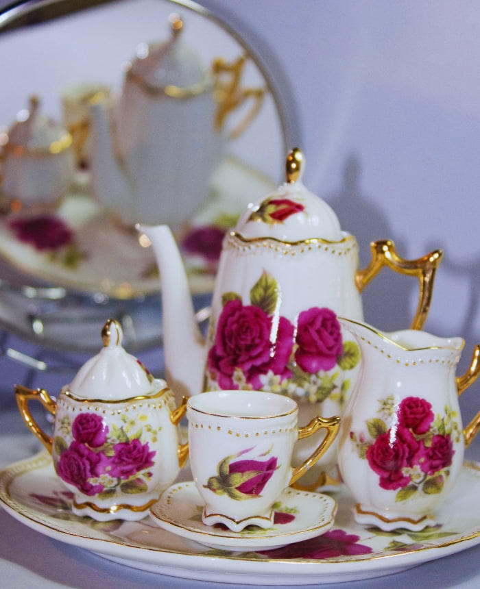 Conjunto de porcelana fina com flores vermelhas e dourado, incluindo bule, xícaras e leiteira