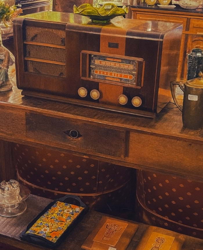 Rádio antigo de madeira sobre aparador clássico, ao lado de vasos, livros e objetos decorativos em um ambiente com móveis antigos